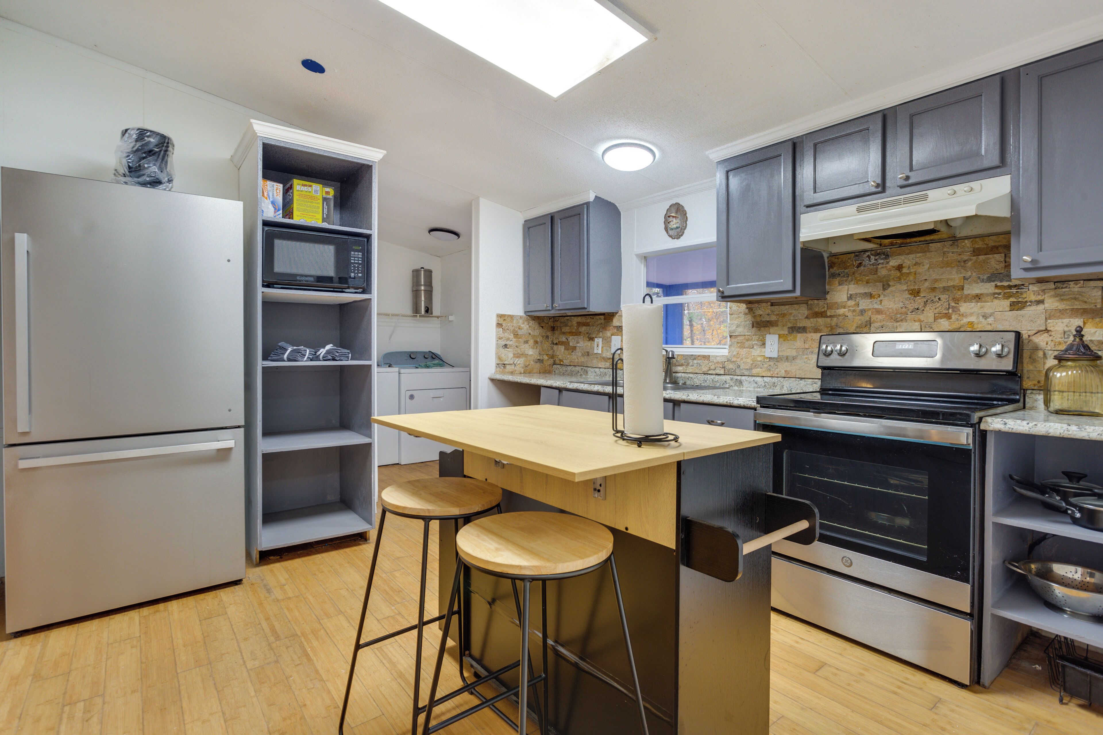 A modern kitchen with grey cabinets, a stainless steel refrigerator, a microwave, a built-in oven, and a wooden island with stools.