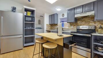 A modern kitchen with grey cabinets, a stainless steel refrigerator, a microwave, a built-in oven, and a wooden island with stools.