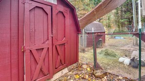 Ein rotes Bauernhaus mit einem Metallgatter und einem eingezäunten Bereich mit Heu und Steinen.