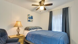 Ein Schlafzimmer mit Bett, Nachttisch, Lampe, Deckenventilator und einem Fenster mit Vorhängen.