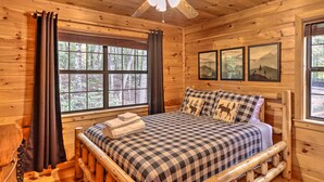 Une chambre dans une cabane en bois, avec un lit, un ventilateur de plafond et des tableaux encadrés accrochés au mur.