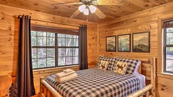 A wooden cabin bedroom with a bed, a ceiling fan, and framed pictures on the wall.