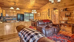 Un intérieur de chalet chaleureux avec un plafond en bois, un fauteuil inclinable en cuir, un coin repas et une cuisine.