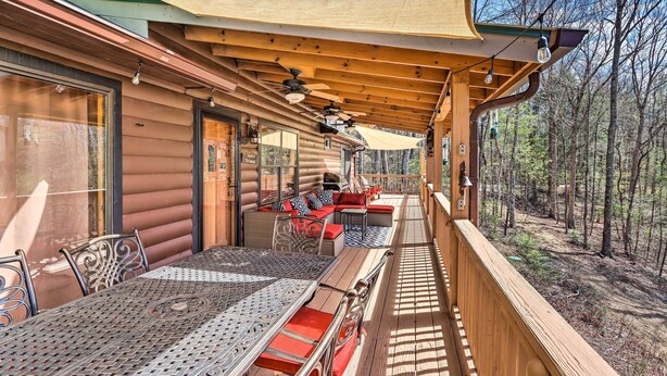 Une terrasse extérieure couverte, dotée d’une table et de chaises, d’un canapé avec des coussins et offrant une vue sur la forêt environnante.