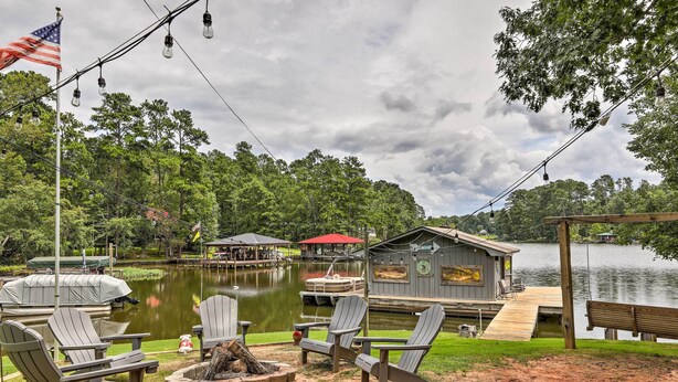 A lakeside deck with Adirondack chairs, a fire pit, and a dock extending into the water. - Lakeside Living: Sparta Retreat w/ Game Room! (Milledgeville)