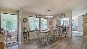 A spacious dining area with a large table and chairs, a kitchen in the background, and a view of the outdoors through large windows. - Lakeside Living: Sparta Retreat w/ Game Room! (Milledgeville)