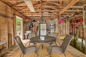 Una terraza de madera con una mesa redonda y cuatro sillas, rodeada de diversos objetos y una pequeña fuente de agua.