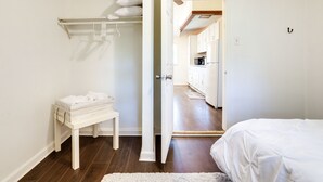 Ein Schlafzimmer mit Bett, Nachttisch, einer weißen Bank und einer Tür zu einer Küchenzeile.