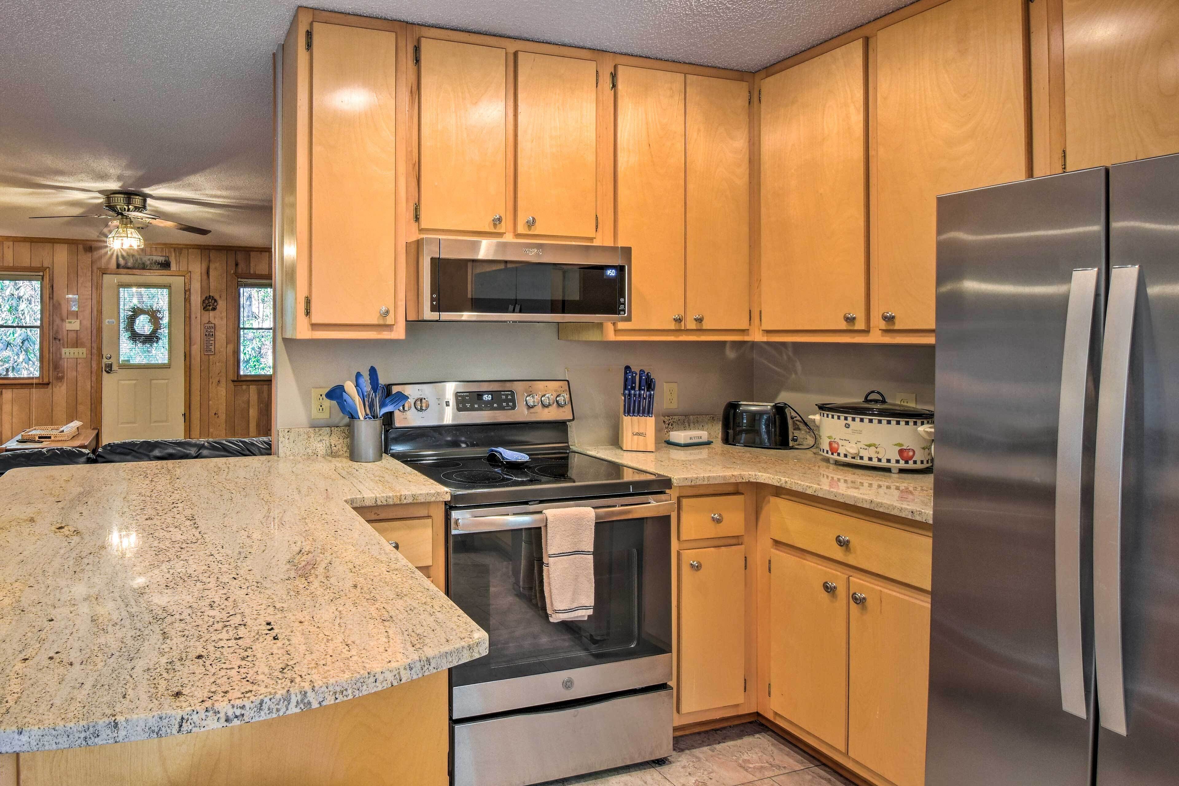 A kitchen with wooden cabinets, a stainless steel refrigerator, a microwave, a stove, and a large granite countertop.