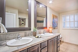 Une salle de bain avec deux lavabos, un grand miroir et une fenêtre avec des stores.