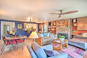 A living room with a sofa, armchairs, a coffee table, and a dining table with chairs. There is a fireplace, a ceiling fan, and a bookshelf with various items. - Tucson House w/ Private Pool: 5 Mi to Downtown! (Tucson)