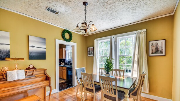 A dining area with a wooden table and chairs, a piano, and a view of the kitchen through an open doorway. - Georgia Vacation Rental: 3 Mi to Downtown Columbus (Columbus)