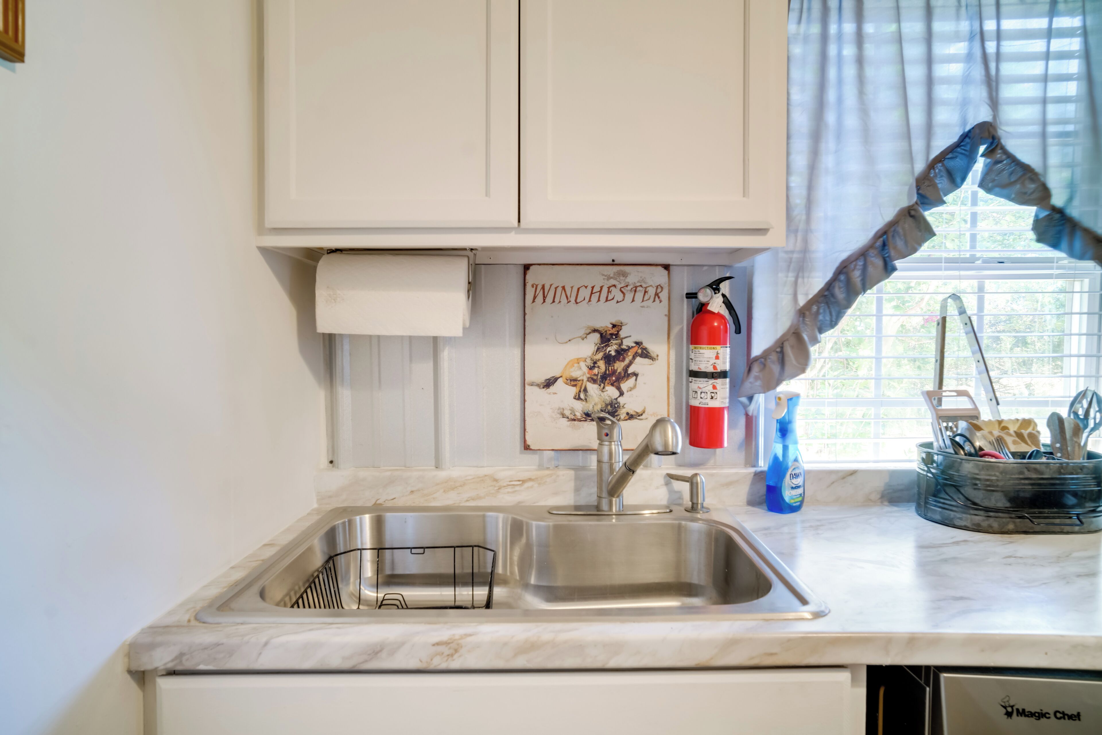 Una cocina con un lavamanos de acero inoxidable, una ventana con persianas, un extintor y un letrero que dice "Winchester".