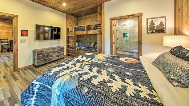 A bedroom with a large bed, wooden bunk beds, a TV, and a bathroom with a glass shower. - Riverside Mtn Retreat w/ Hot Tub & Game Room! (Blue Ridge)