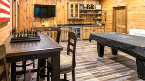 A wooden-themed room with a chessboard, a bed, a TV, and a kitchen area. - Riverside Mtn Retreat w/ Hot Tub & Game Room! (Blue Ridge)