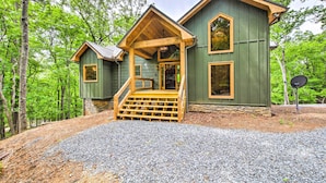 A cabin with a wooden porch and a stone foundation, surrounded by trees. - Riverside Mtn Retreat w/ Hot Tub & Game Room! (Blue Ridge)