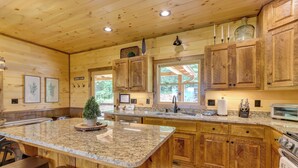 A wooden cabin-style kitchen with granite countertops, wooden cabinets, and a central island with bar stools.