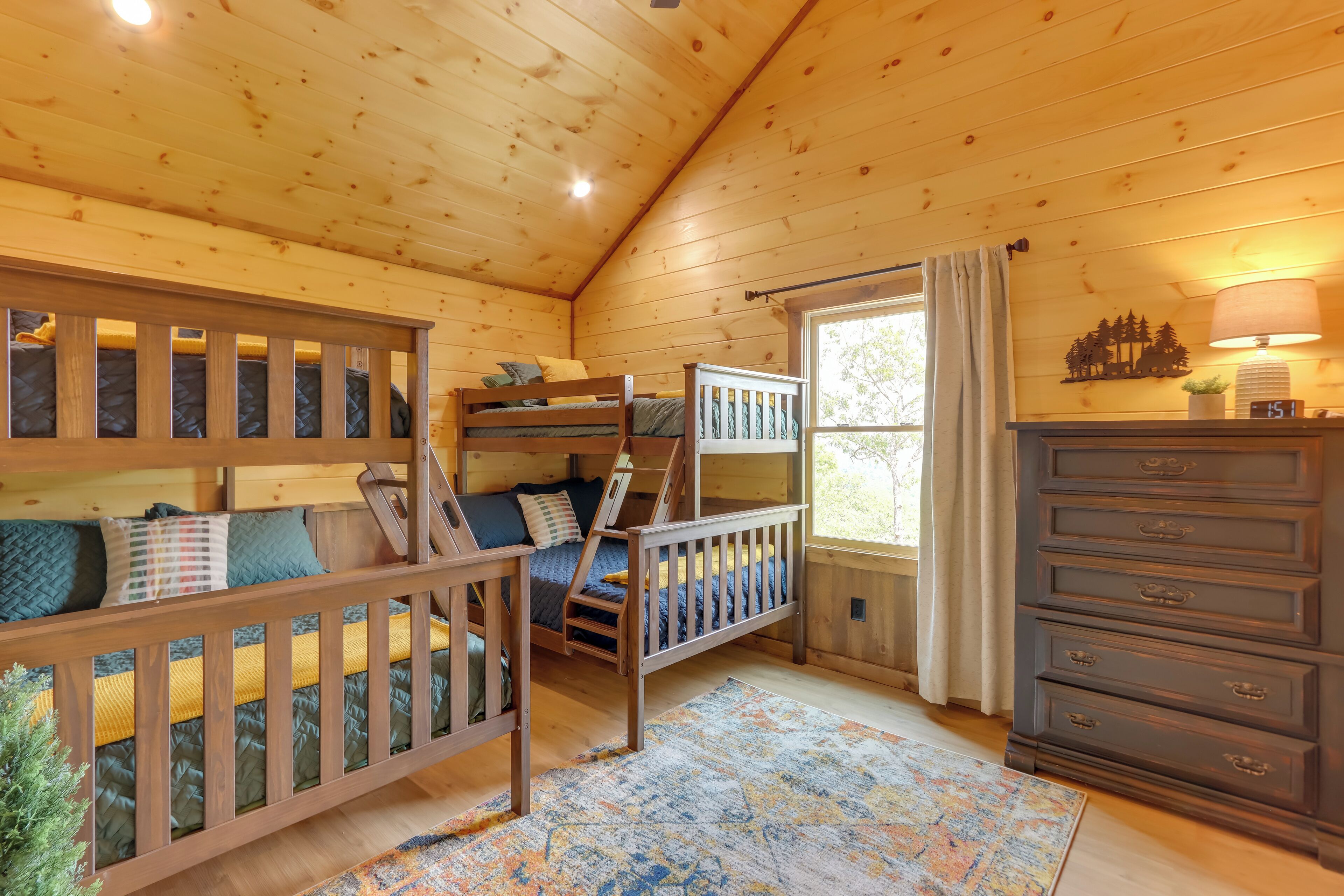 A cozy cabin room with bunk beds, a dresser, and a window with curtains.