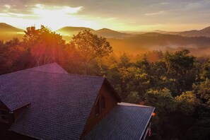 A house with a sloped roof, surrounded by dense forest and hills.