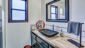 Une salle de bain avec un meuble-lavabo en bois, un grand miroir, une fenêtre et un panneau indiquant la Route 66.