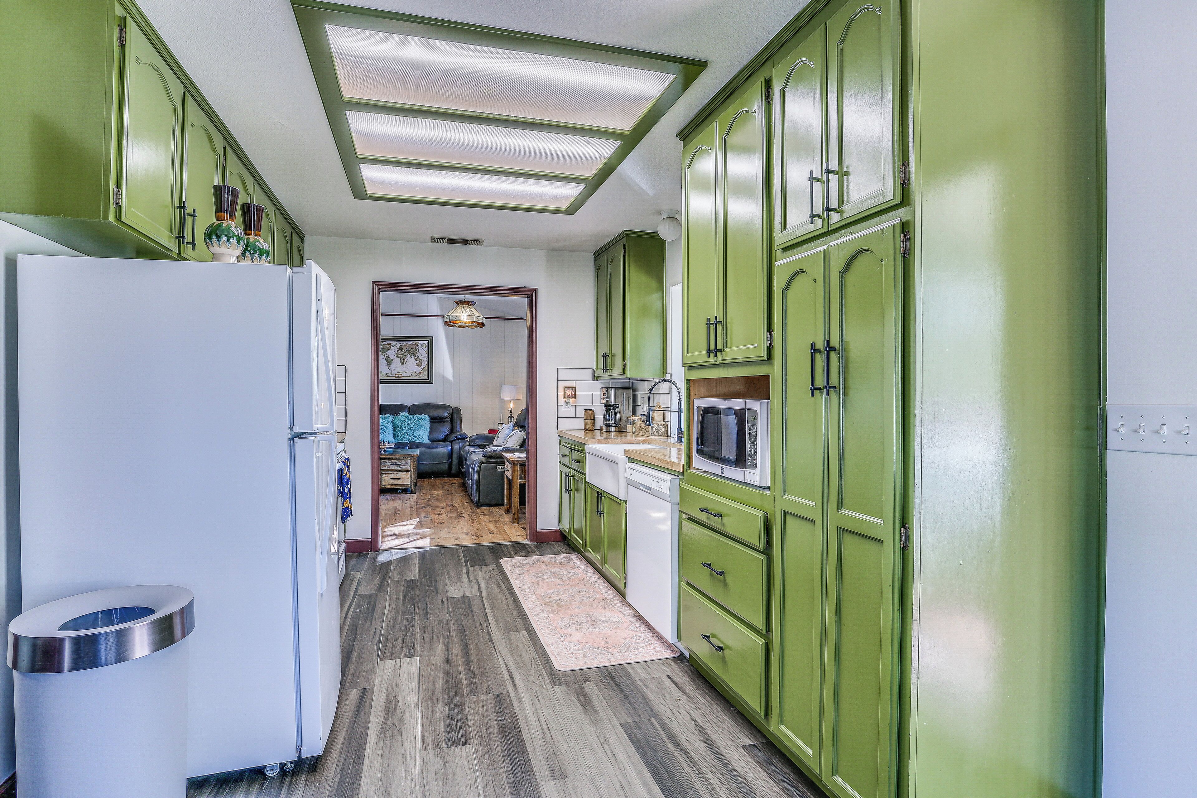 Una cocina con armarios verdes, un refrigerador blanco y un microondas.