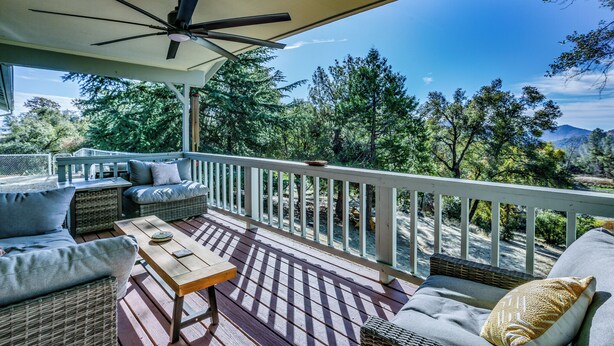 Une terrasse extérieure couverte, aménagée avec des meubles en osier, un ventilateur de plafond et offrant une vue sur une zone boisée.
