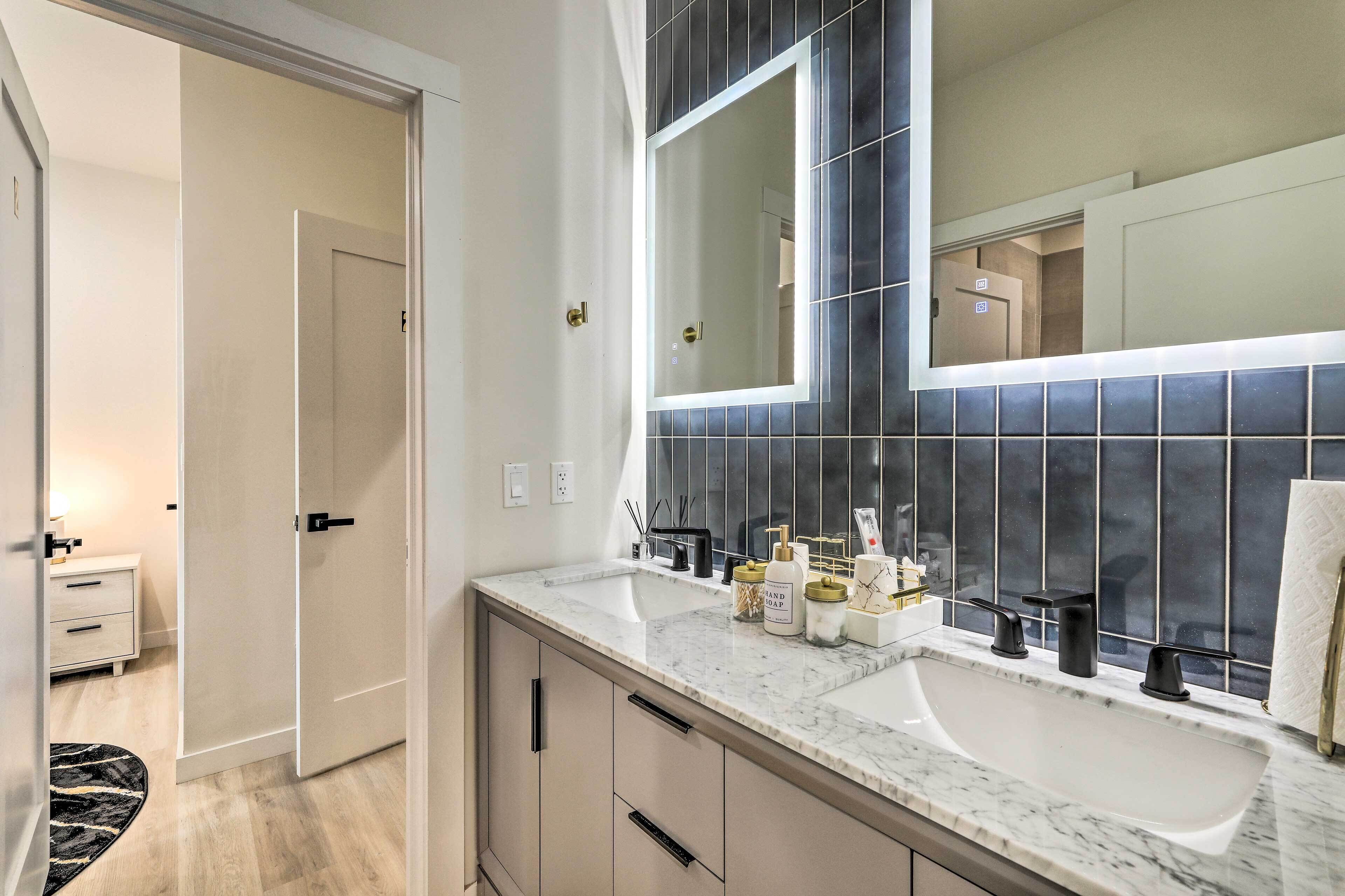 A bathroom with a large mirror, dark tiled backsplash, and a white sink with two faucets.