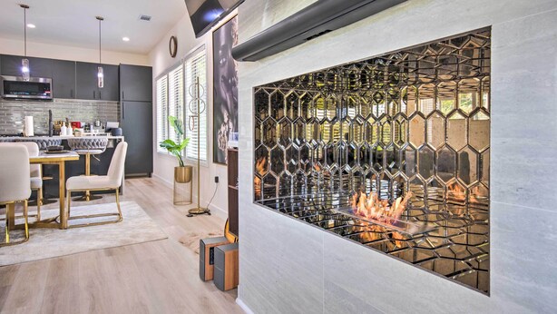 A modern kitchen with a built-in fireplace, a dining area with a white table and chairs, and a large window with a geometric metal screen. - Luxury Smart Home: 2 Mi to Downtown Atlanta! (Atlanta)
