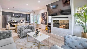 A modern kitchen with a dining area, a fireplace, and a large TV mounted on the wall. - Luxury Smart Home: 2 Mi to Downtown Atlanta! (Atlanta)