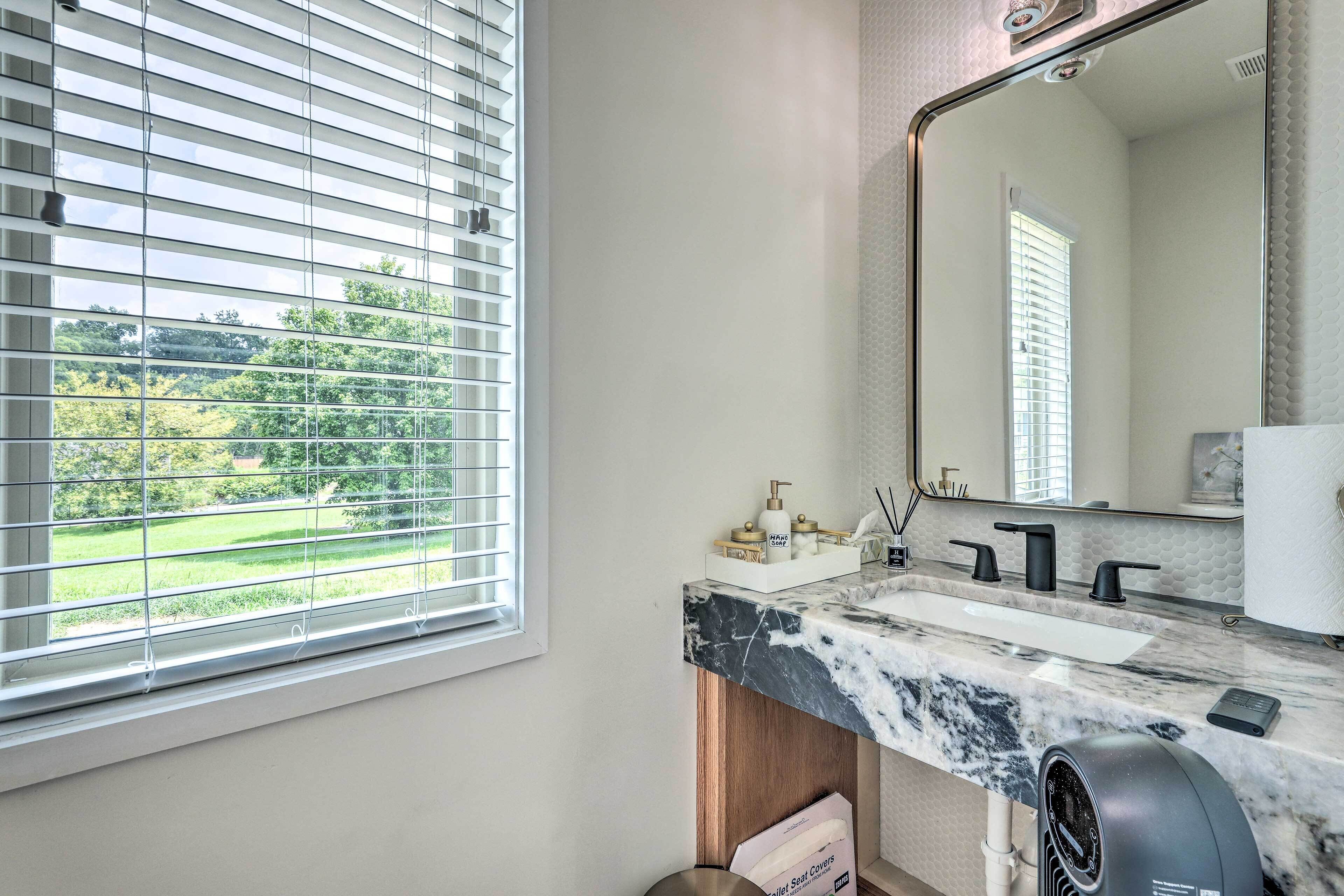 A bathroom with a large window, a marble countertop, a sink, a mirror, and a hair dryer.