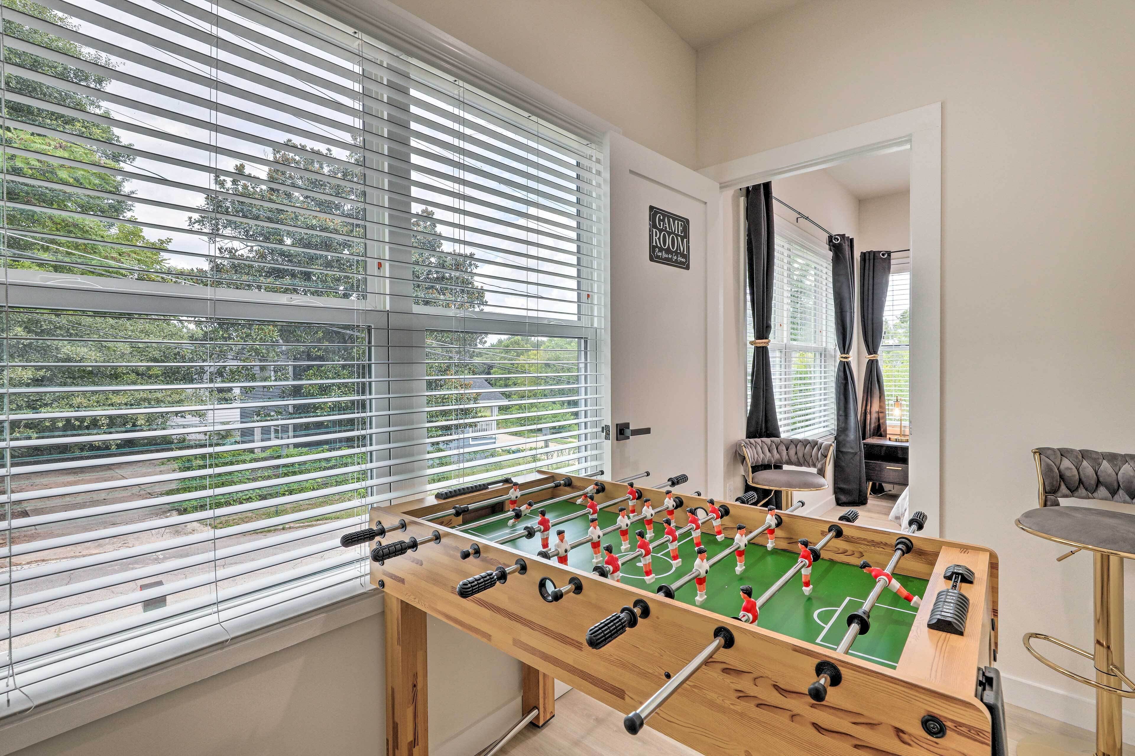 A foosball table in a room with a view through large windows, a sign reading "GAME ROOM," and a door leading to another area.