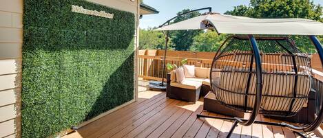 Eine Holzterrasse mit grüner Wand und einem Schaukelsessel.