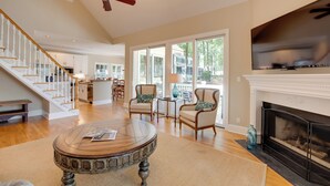 A spacious living room with a fireplace, a television mounted above it, a round coffee table, and a staircase leading to the upper floor. - Stunning Lake Oconee Retreat w/ Pool Access! (Eatonton)
