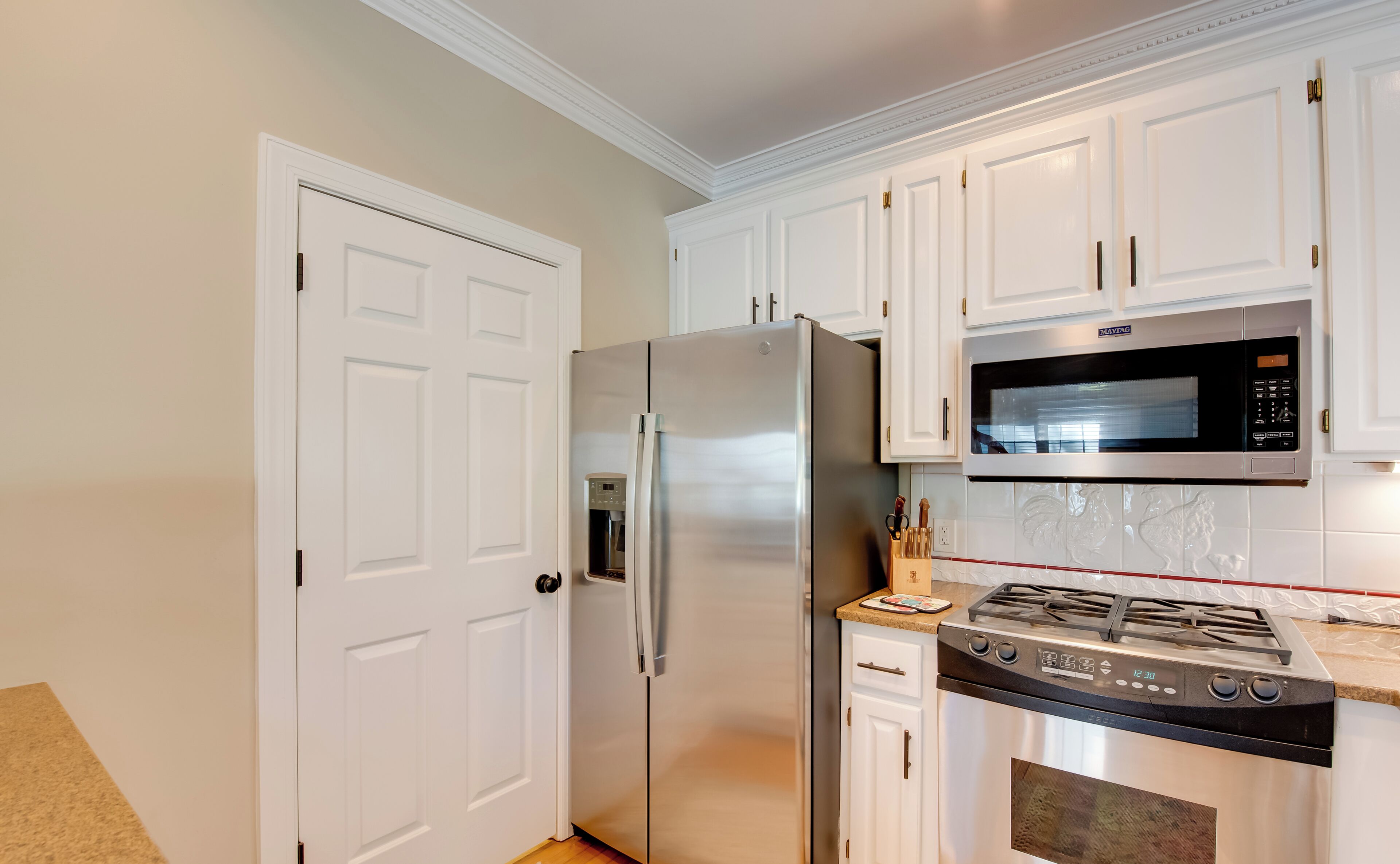 A modern kitchen with white cabinetry, a stainless steel refrigerator, a built-in microwave, and a gas stove.