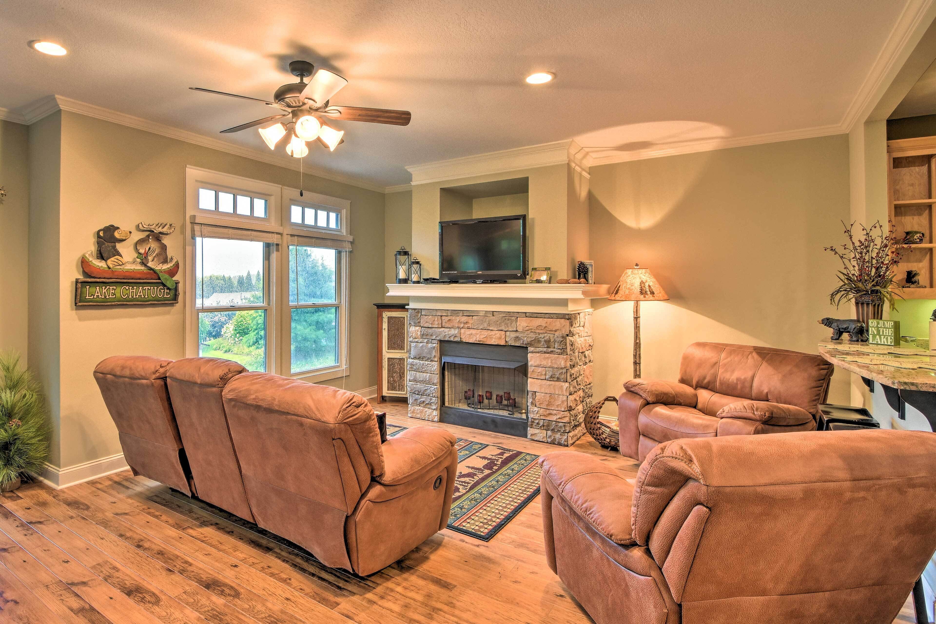A living room with a stone fireplace, leather recliners, a television, and a ceiling fan.