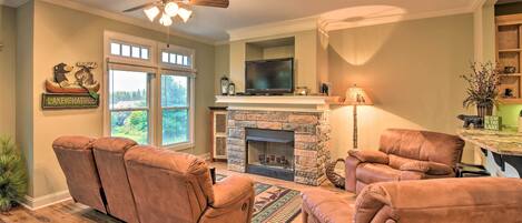 A living room with a stone fireplace, leather recliners, a television, and a ceiling fan.