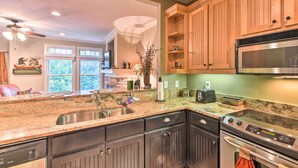 A kitchen with granite countertops, stainless steel appliances, wooden cabinets, and a view of the outdoors through large windows. - Hiawassee Haven on Lake Chatuge w/ Boat Slip! (Hiawassee)