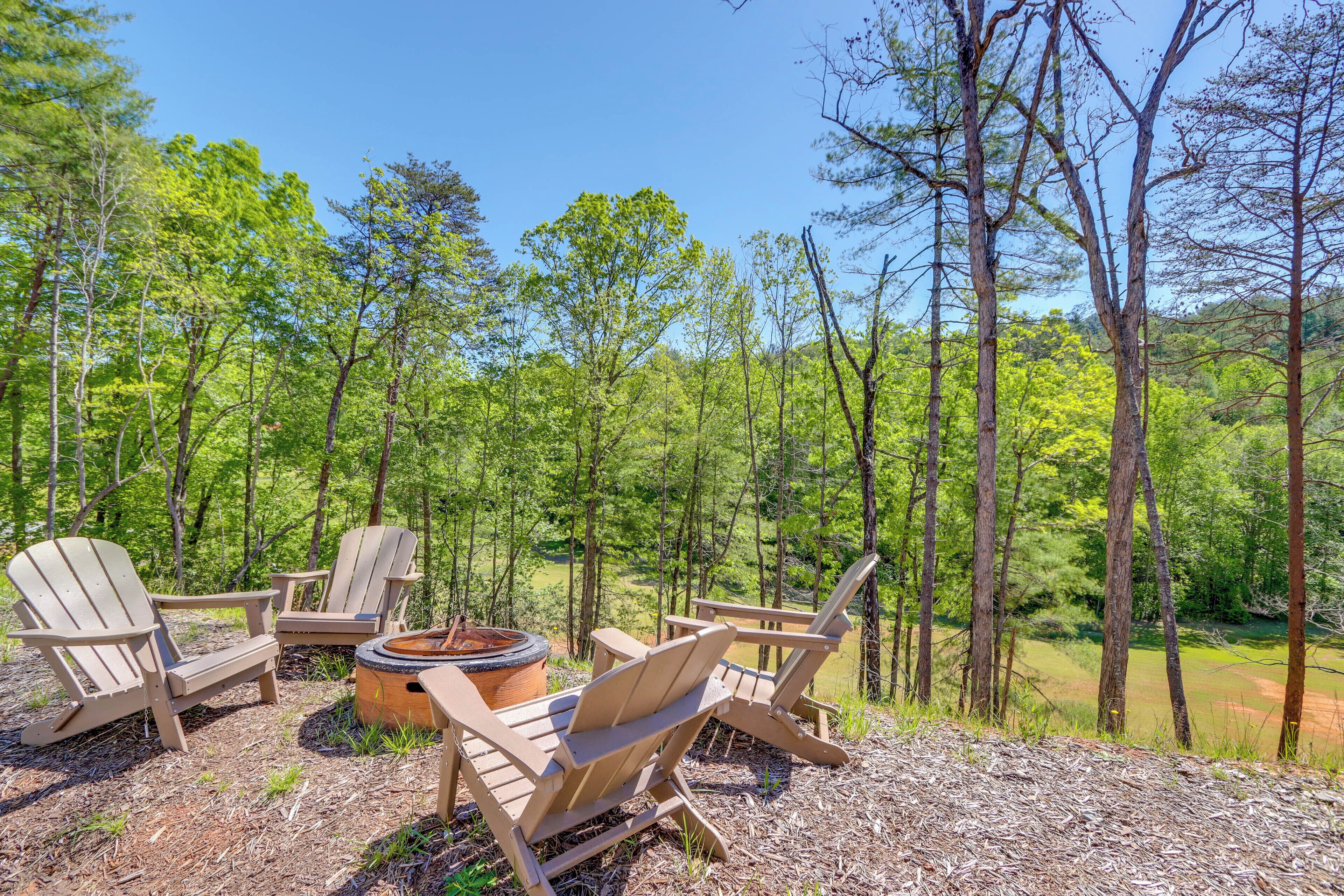 Un espacio al aire libre con sillas Adirondack y una fogata, rodeado por un bosque.