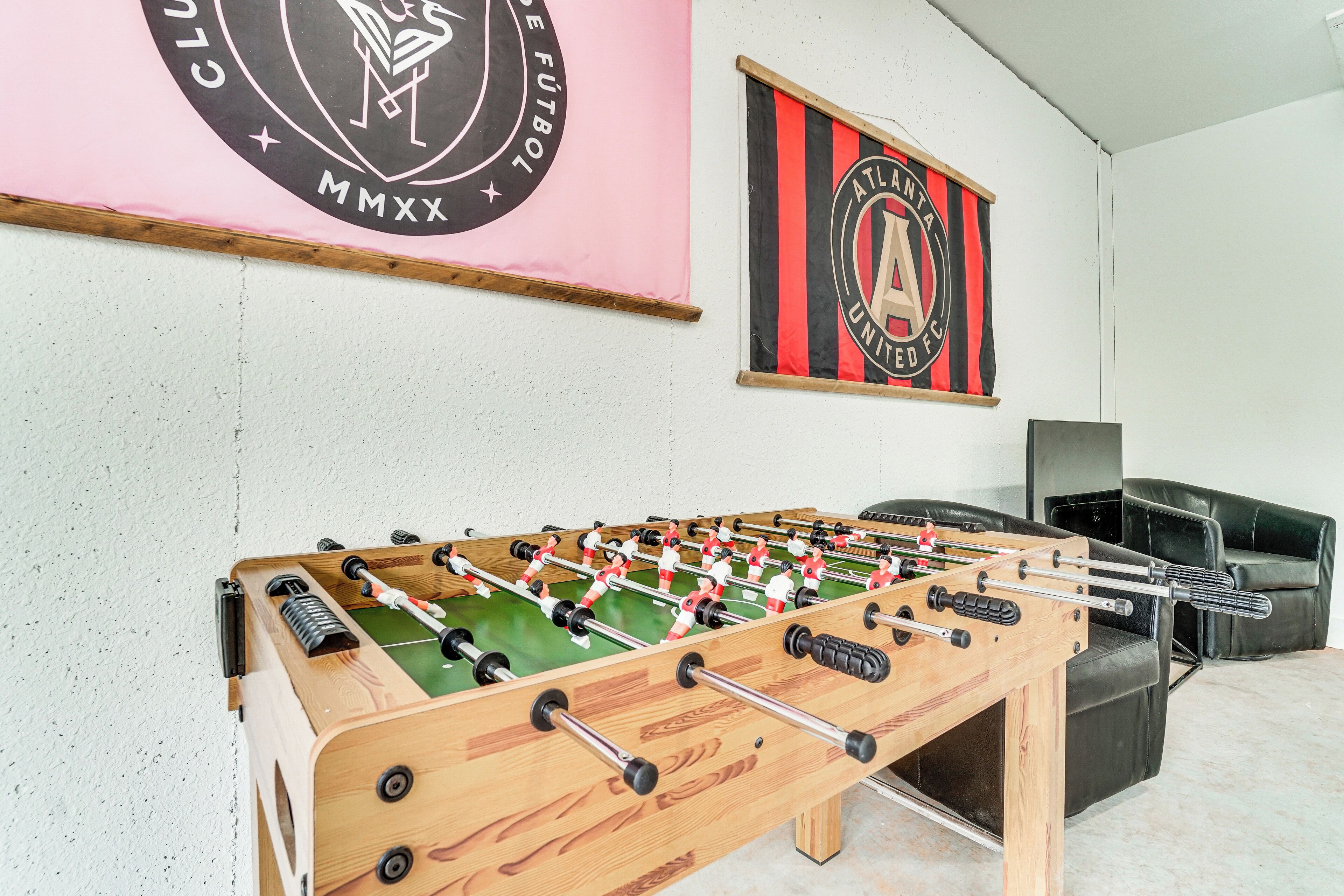 A foosball table in a room with a white wall, a black leather couch, and two banners with club logos.