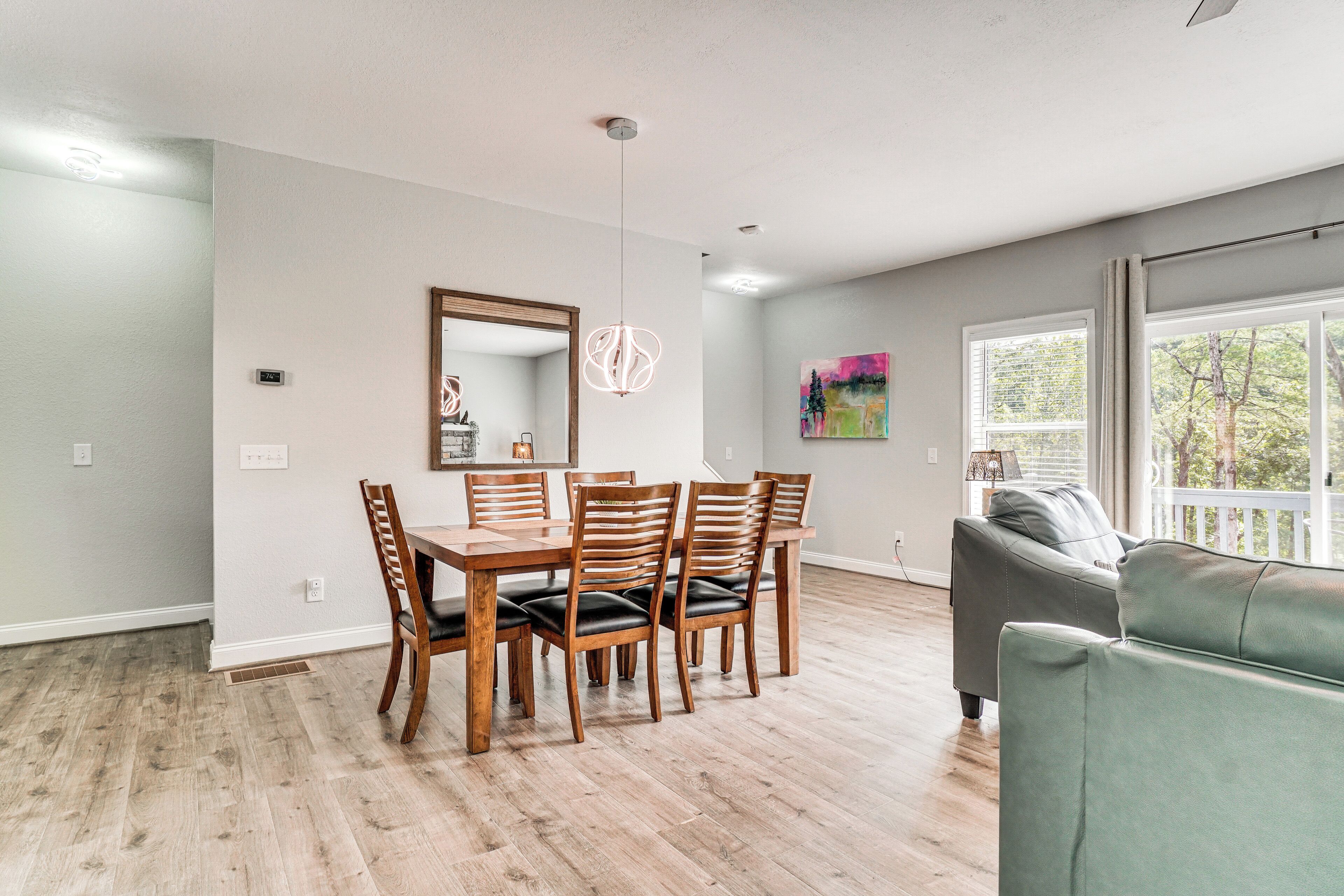 A dining area with a wooden table and chairs, a pendant light, a large mirror, and a painting on the wall.