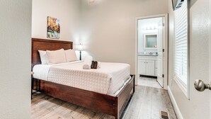 Quarto com cama de madeira, ventoinha no teto, pintura na parede e banheiro visível através de uma porta aberta.
