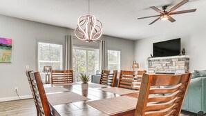 Uma área de jantar com mesa de madeira, cadeiras, ventilador de teto e lareira de pedra.