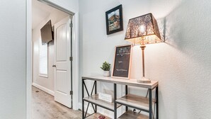 Um corredor com um console de madeira, uma luminária fixada na parede e um letreiro com uma mensagem motivacional.