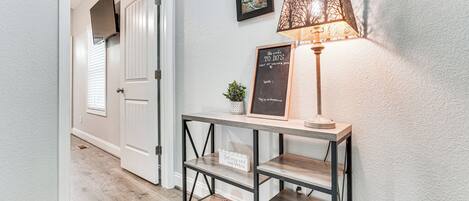 A hallway with a wooden console table, a wall-mounted lamp, and a sign with a motivational message.