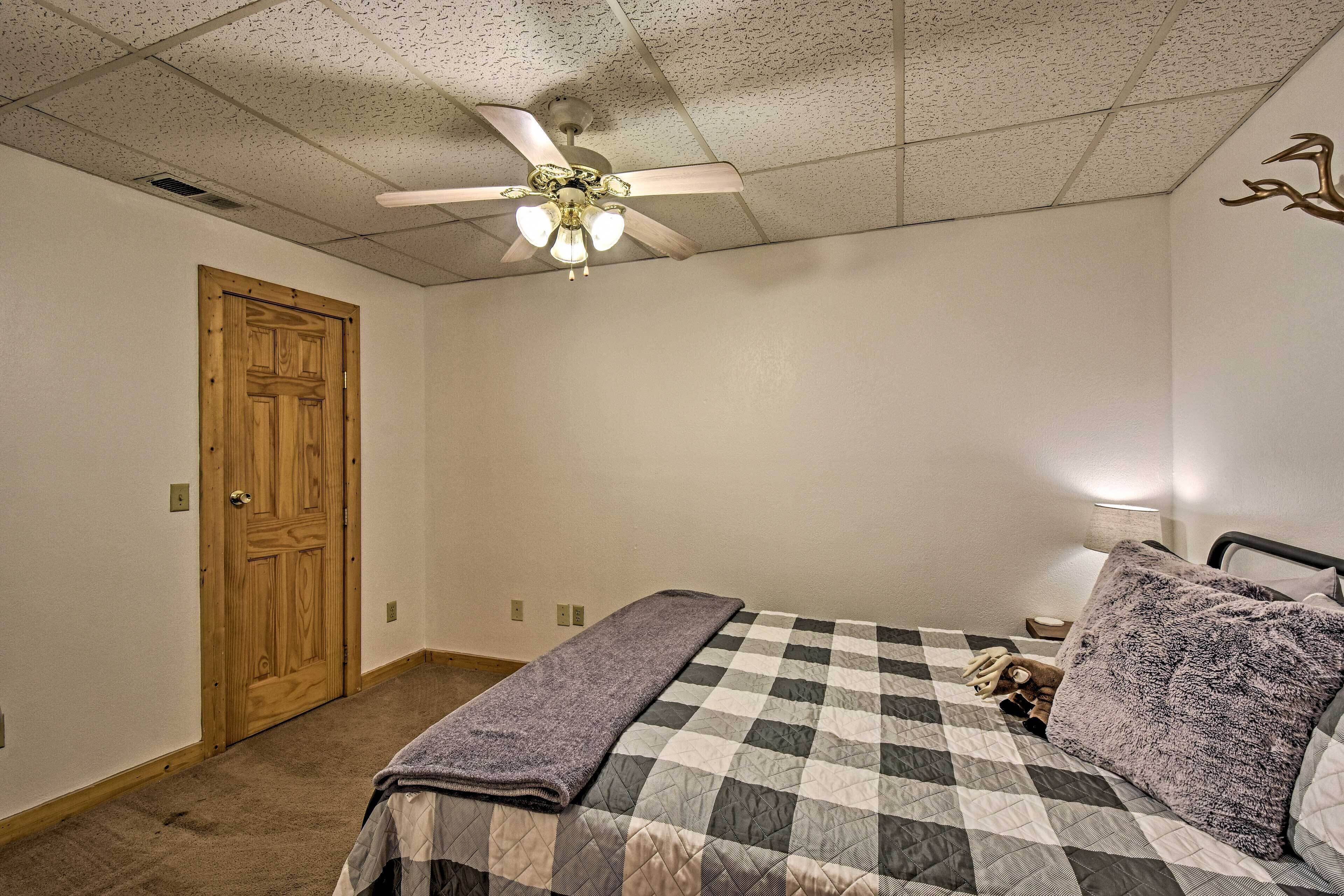 A bedroom with a bed, a ceiling fan, a wooden door, and a nightstand with a lamp.