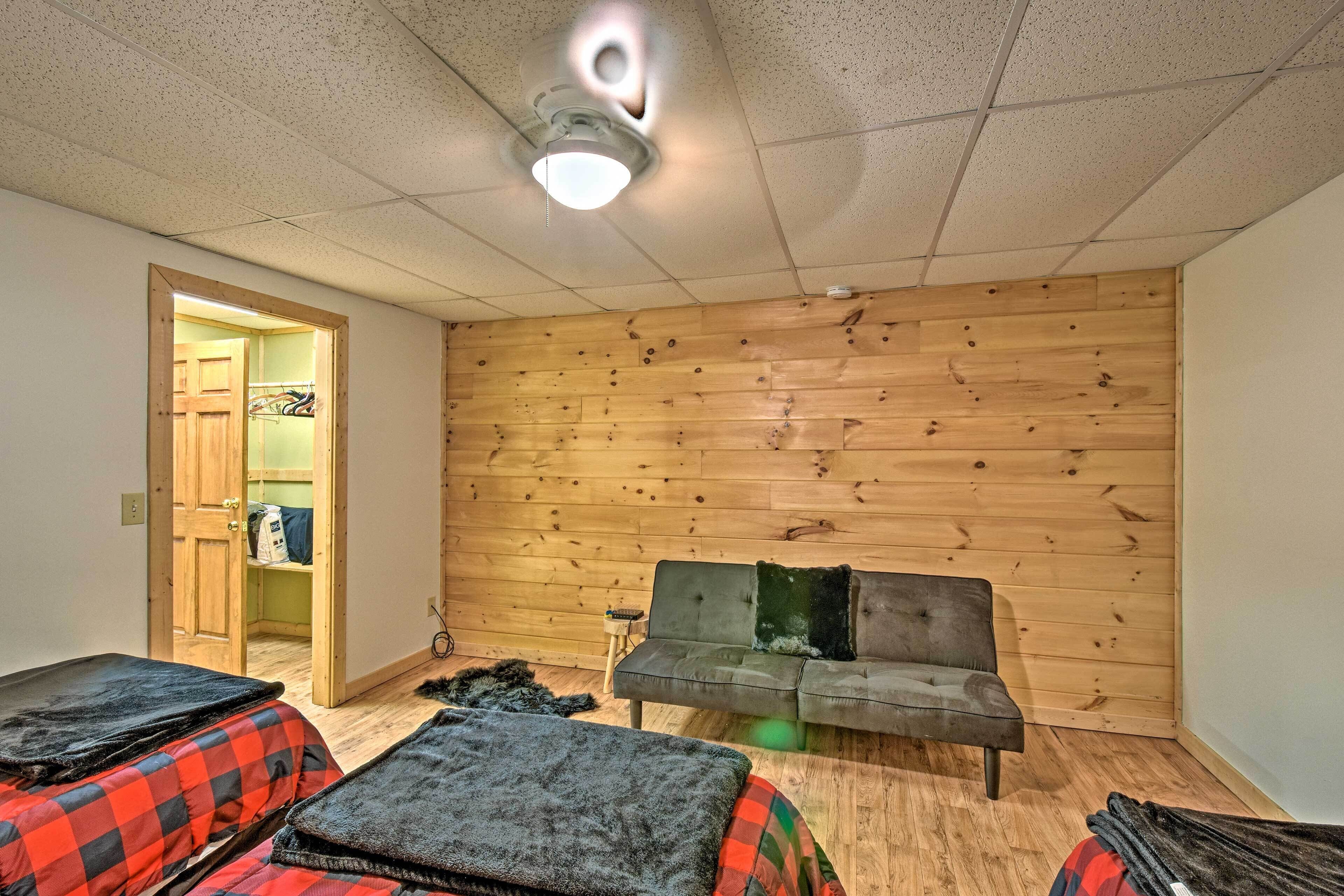 Ein Zimmer mit Holzwand, einem grauen Sofa und zwei Betten mit rot-schwarz karierter Bettwäsche.