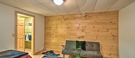 Ein Zimmer mit Holzwand, einem grauen Sofa und zwei Betten mit rot-schwarz karierter Bettwäsche.