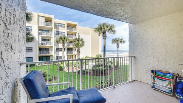 A balcony with a view of a building, palm trees, and a beach. - New Smyrna Beach Condo w/ Ocean-view Balcony! (New Smyrna Beach)