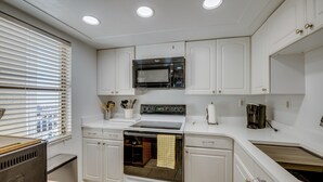 A modern kitchen with white cabinetry, a built-in microwave, oven, and sink. - New Smyrna Beach Condo w/ Ocean-view Balcony! (New Smyrna Beach)