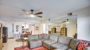 A living room with a sectional sofa, a dining table, and chairs. There is a ceiling fan and a large mirror on the wall. - New Smyrna Beach Condo w/ Ocean-view Balcony! (New Smyrna Beach)
